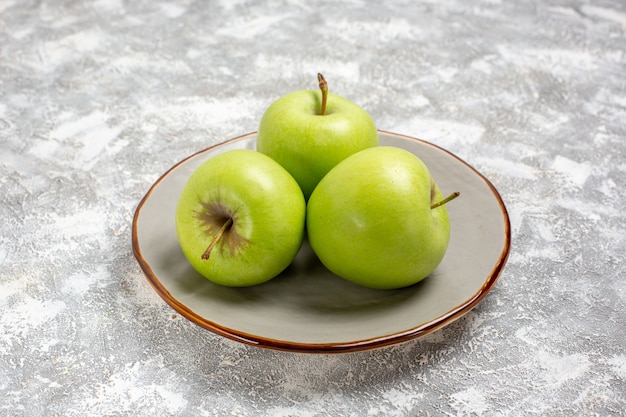 Vista frontale mele verdi fresche all'interno del piatto sulla superficie bianco-chiaro vitamina fresca e matura di frutta fresca