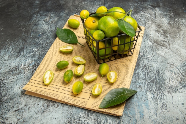 Front view of fresh kumquats and lemons in a black basket on newspapers on gray background stock image