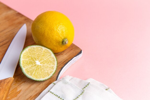 Front view of fresh lemon with sliced lime on the pink wall