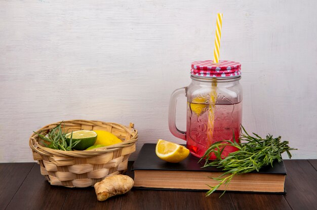 Front view of fresh lemons on a bucket with tarragon with lemon juice in a glass jar on white surface