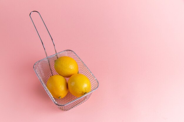 Front view of fresh lemons citruses inside fryer on the pink wall