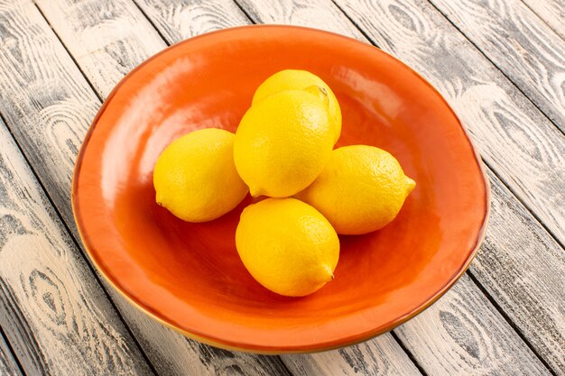 A front view fresh lemons sour ripe mellow juicy citrus inside orange plate vitamine yellow on the grey rustic desk