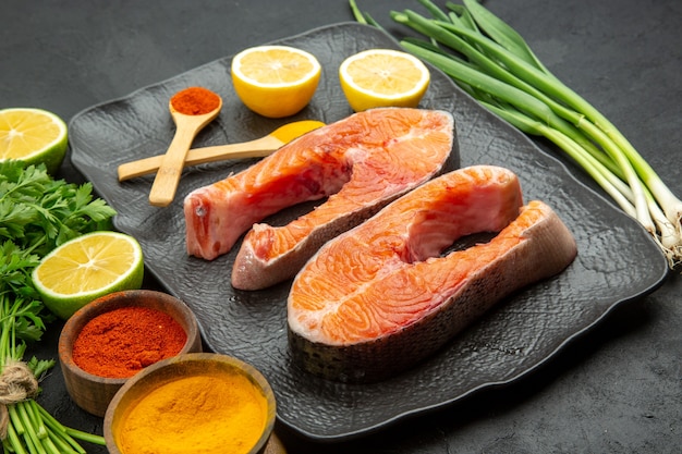 Вид спереди кусочки свежего мяса с зеленью лимона и приправами на темном фоне блюдо еда рыба фото ребра животная еда