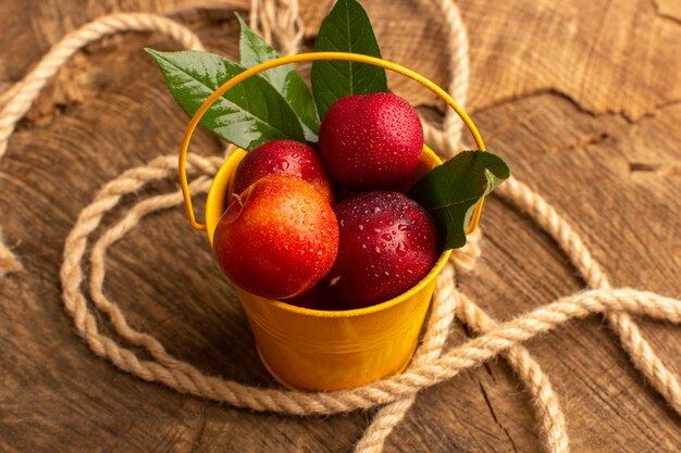 Front view fresh mellow plums inside yellow basket along with ropes on wooden desk