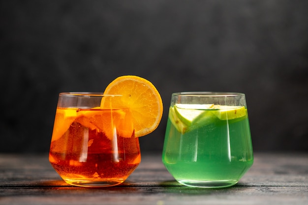 Вид спереди свежего натурального вкусного сока в двух стаканах с фруктовым лаймом на черном фоне