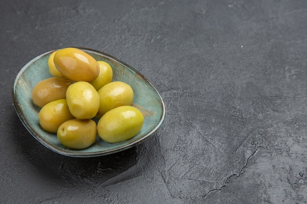 Front view of fresh organic green olives on a blue plate on a black background