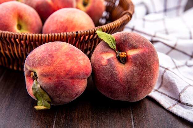 Front view of fresh peaches on a bucket with peaches isolated on a checked tablecloth on a wooden surface