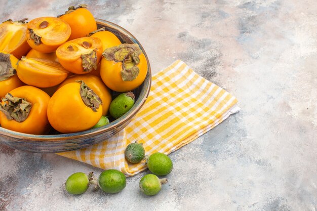Front view fresh persimmons in a bowl yellow kitchen towel feykhoas on nude