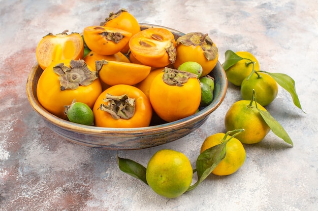 Вид спереди свежие фейхоа хурмы в миске и мандарины на обнаженном фоне