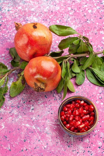 Foto gratuita melograno fresco vista frontale con foglie verdi sulla superficie rosa