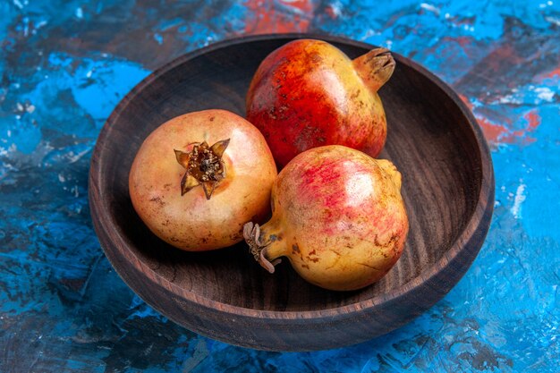 Front view fresh pomegranates in wooden bowl on blue