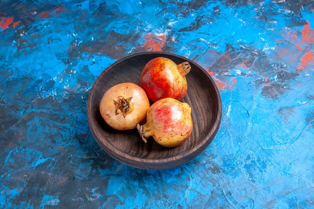 Front view fresh pomegranates in wooden bowl on blue