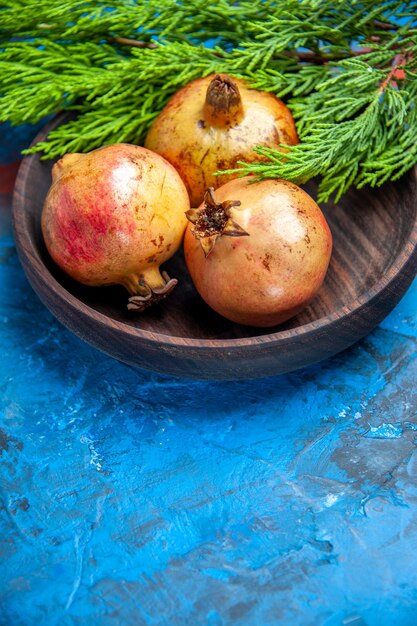 Front view fresh pomegranates in wooden bowl pine tree branch on blue background with copy space