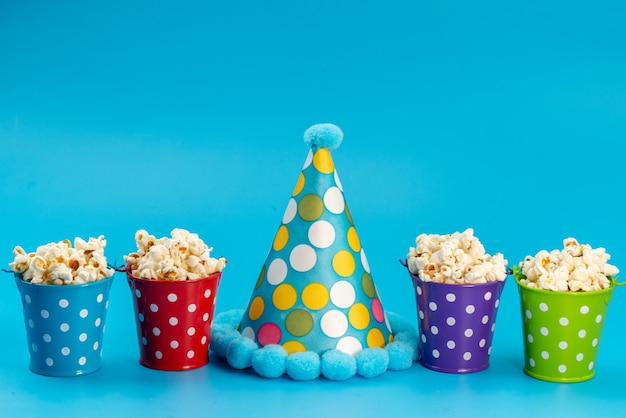 Вид спереди свежий попкорн в разноцветных корзинах вместе с кепкой для дня рождения на синем, кукуруза для снеков из кино