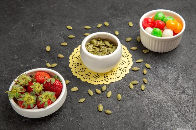 Front view fresh pumpkin seeds with candies and strawberries on grey background seed color rainbow candy fruit