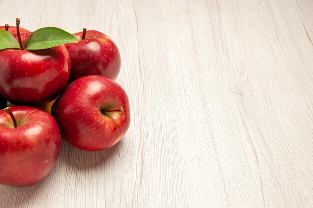 Вид спереди свежие красные яблоки, спелые и спелые фрукты на белом столе, цвет фруктов, свежее растение, красное дерево