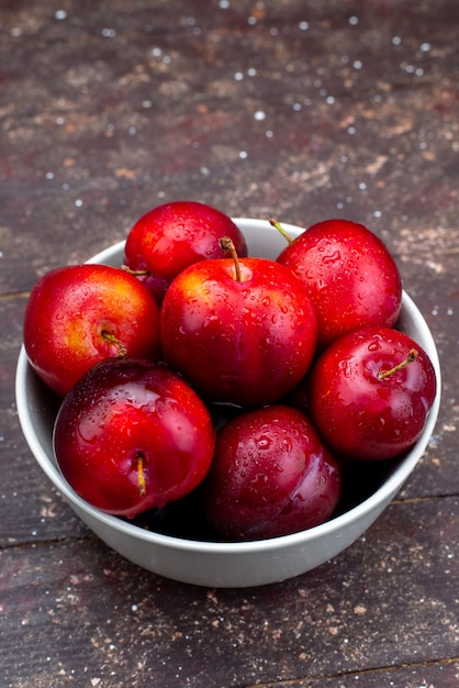 Foto gratuita una prugne rosse fresche di vista frontale mellow e mature all'interno del piatto bianco sul succo di frutta in legno dello scrittorio