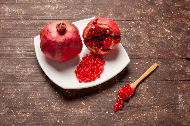 Front view fresh red pomegranates inside plate on brown rustic desk