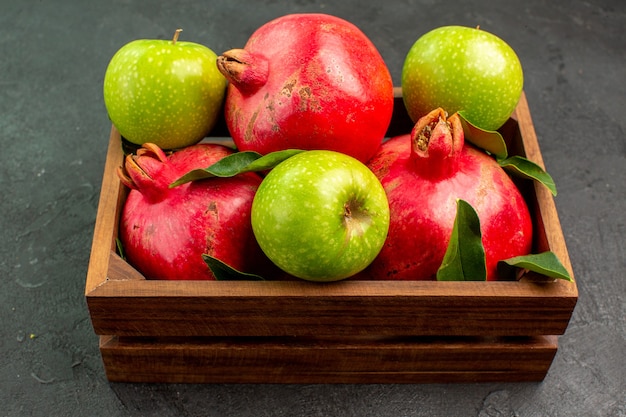 Вид спереди свежие красные гранаты с зелеными яблоками на темной поверхности цвета спелых фруктов