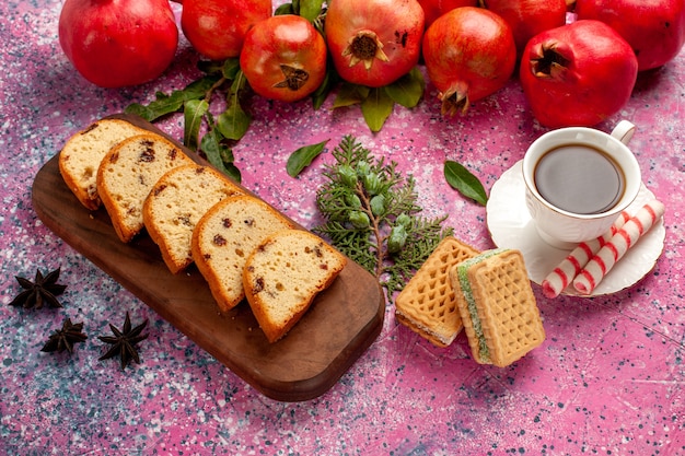 Melograni rossi freschi di vista frontale con tè e cialde della torta affettata sulla scrivania rosa