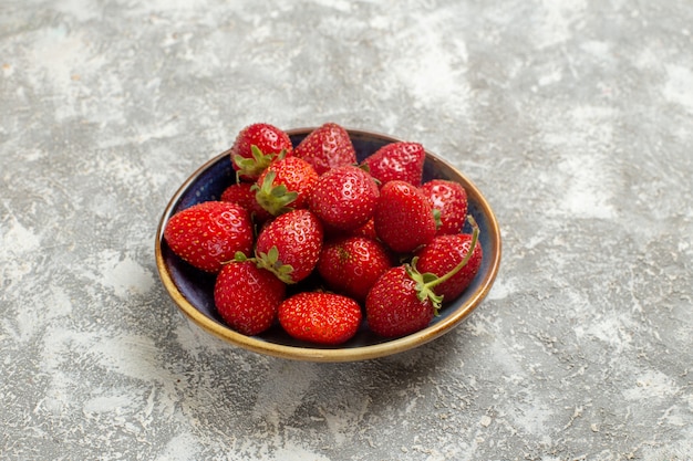 Вид спереди свежей красной клубники внутри тарелки на белом столе красные ягоды свежие фрукты