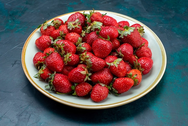 Вид спереди свежей красной клубники, спелых фруктов, ягод внутри тарелки на темно-синей поверхности, ягодных фруктов, спелого лета