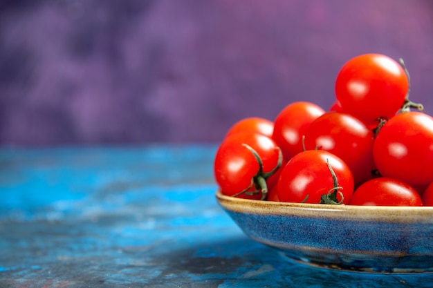 파란색 테이블에 있는 접시 안에 있는 신선한 빨간 토마토 전면 보기