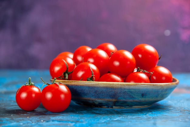 Вид спереди свежие красные помидоры внутри тарелки на синем столе