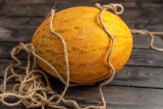 Front view fresh ripe melon whole orange ed with ropes on the brown rustic background