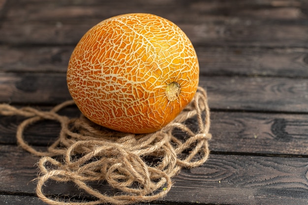 Front view fresh ripe melon whole orange ed with ropes on the brown rustic desk