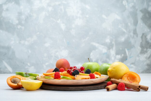 正面の新鮮なスライスフルーツのまろやかさとビタミンが豊富なシナモンと木製の机の上の果物全体と白い背景の果物色食品写真