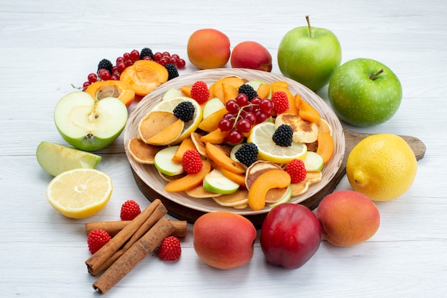 A front view fresh sliced fruits mellow with cinnamons and whole fruits on the wooden desk and white background fruits color food photo