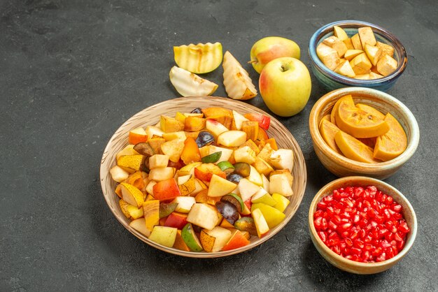 Front view fresh sliced fruits with pomegranates on a dark-grey table many fruits health