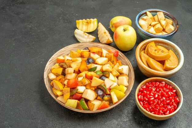 Свежие нарезанные фрукты с гранатами на темно-сером столе, вид спереди, здоровье многих фруктов