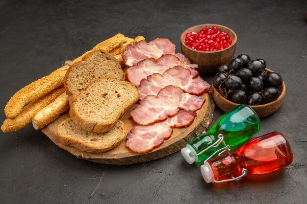 Вид спереди свежей нарезанной ветчины с булочками, фруктами и ломтиками хлеба на темной еде, цветная еда, мясо, закуска, свинья