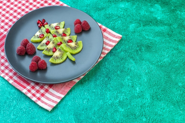 Свежий нарезанный киви с малиной на зеленой поверхности, вид спереди, ягоды, экзотические фрукты, фото тропического цвета