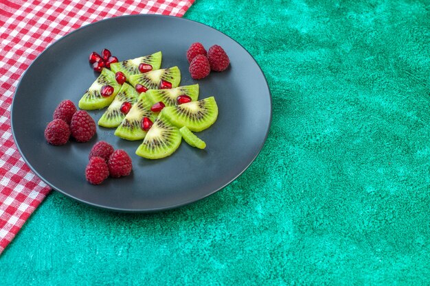 Вид спереди свежесрезанный киви с малиной внутри тарелки на зеленой поверхности фото экзотический сок тропических фруктов цвет ягоды