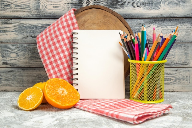 Вид спереди свежие нарезанные апельсины с блокнотом и карандашом на сером фоне фруктовая цитрусовая тетрадь цвета
