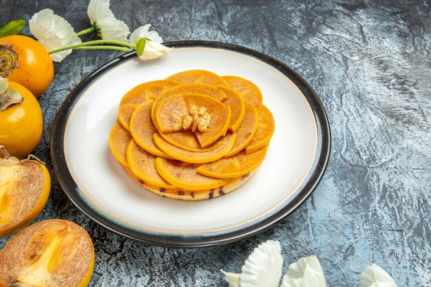 Front view of fresh sliced persimmons inside plate on dark surface