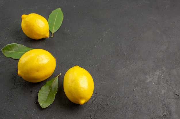 Свежие кислые лимоны, вид спереди, выложенные на темном фоне