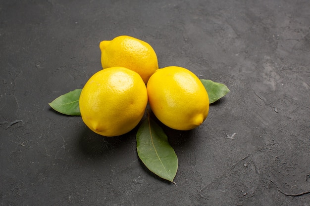 Свежие кислые лимоны с листьями на темном фоне, вид спереди