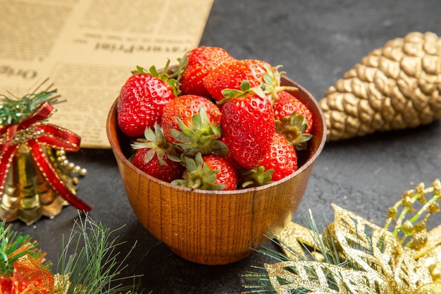 어두운 배경 사진에 있는 크리스마스 장난감 주위의 접시 안에 있는 신선한 딸기는 많은 과일 색을 부드럽게 합니다.