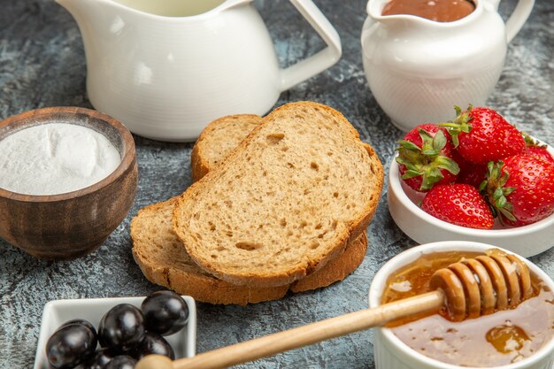 Вид спереди свежей клубники с чаем, хлебом и медом на темной поверхности фруктовой сладкой еды