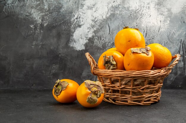 Vista frontale di cachi dolci freschi all'interno del cesto sul tavolo scuro