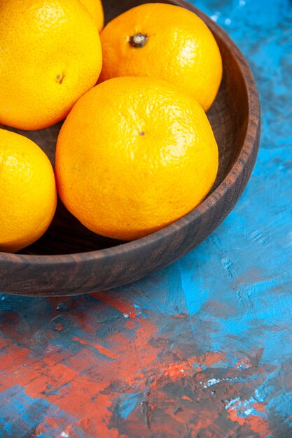 Вид спереди свежие мандарины внутри тарелки на синем столе