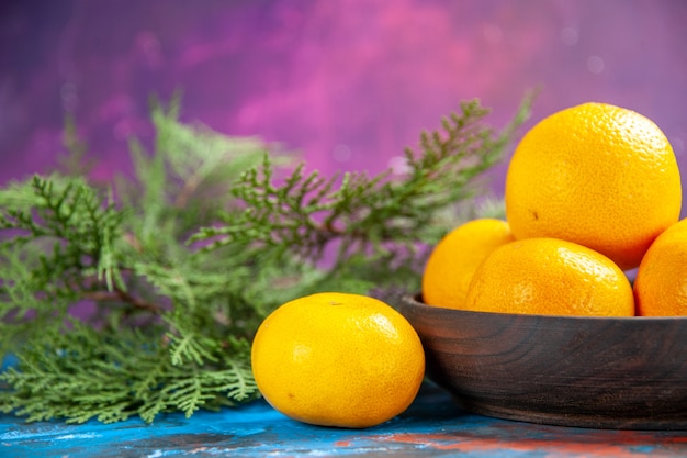 Front view fresh tangerines inside plate with green branches on a blue table 