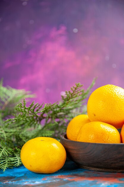 Front view fresh tangerines inside plate with green branches on blue table