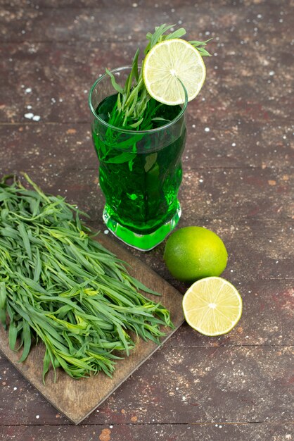 Front view fresh tarragon drink inside long glass with fresh tarragon leaves on brown, tarragon green drink juice