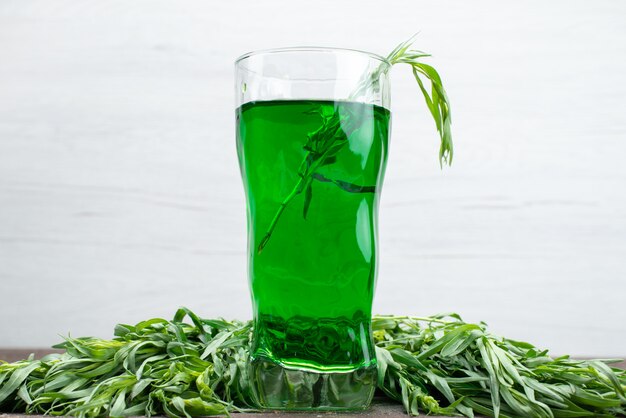 Front view fresh tarragon drink inside long glass with fresh tarragon leaves on white, tarragon green drink juice