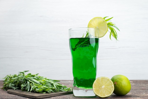 Front view fresh tarragon drink inside long glass with lemons and fresh tarragon leaves on white, tarragon green drink juice